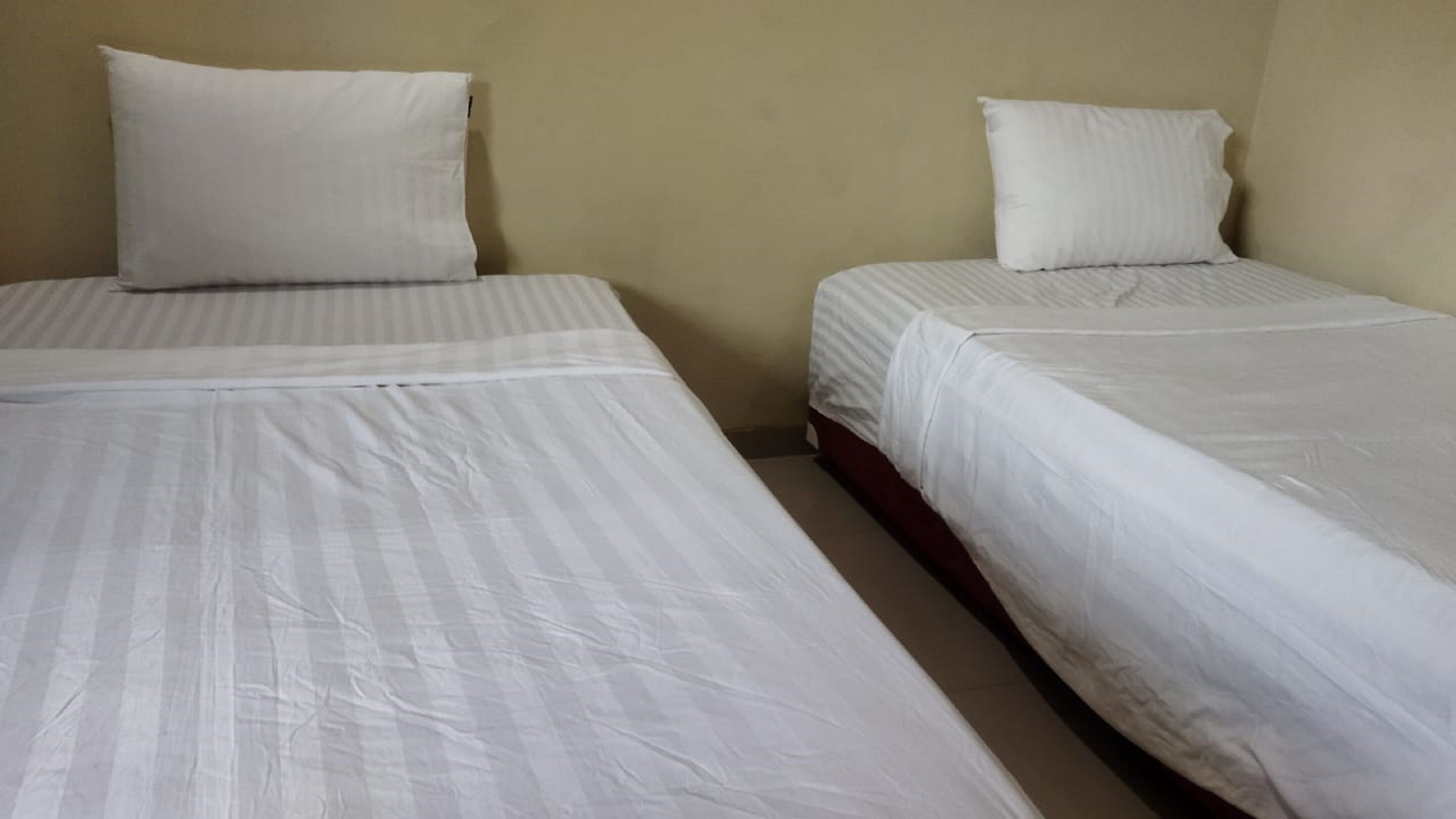 Two single beds with white linens in a room with beige walls.