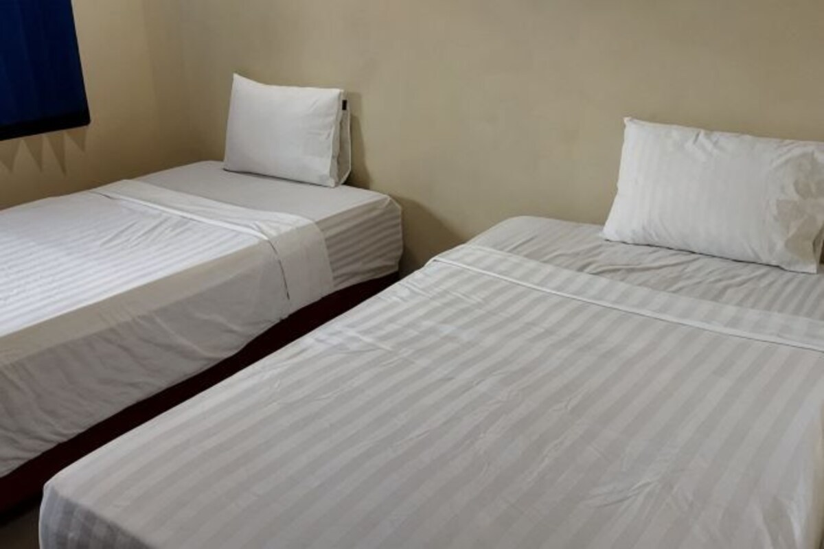 Two single beds with white bedding in a room with plain walls.