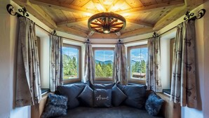 A cozy room with a wooden ceiling, a large window with a view of mountains, and a dark-colored sofa with a decorative pillow. - Appartement Kehlstein für 2 Personen, 38qm mit Balkon (Schönau am Königssee)