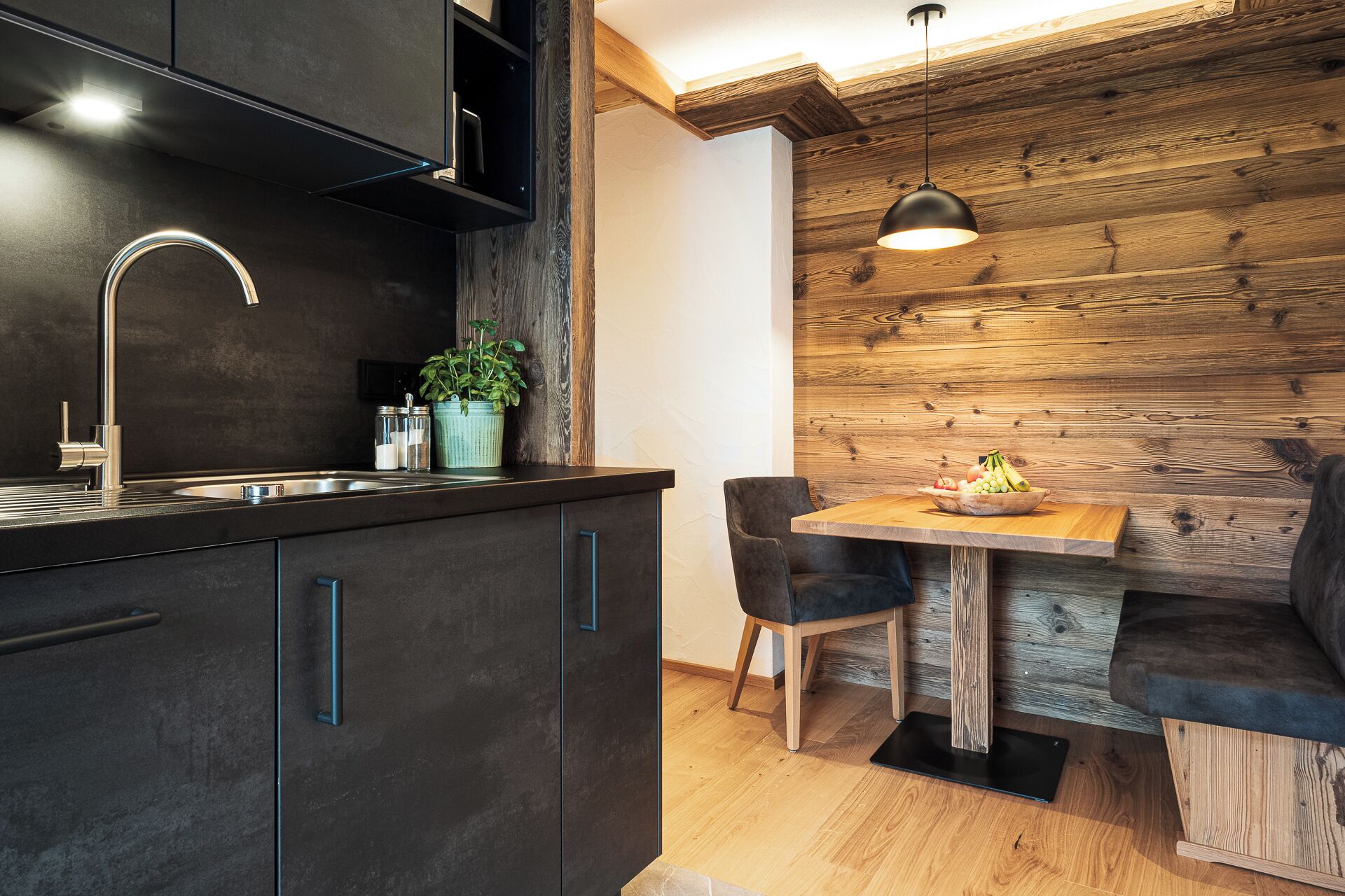 A modern kitchen with dark cabinetry, a stainless steel sink, and a wooden dining area with a table and chairs.