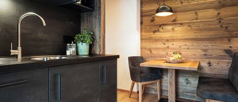 A modern kitchen with dark cabinetry, a stainless steel sink, and a wooden dining area with a table and chairs.
