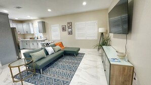 A modern living room with a grey sectional sofa, a patterned rug, a glass coffee table, and a TV mounted on the wall. - Guesthouse near Anaheim Convention (Santa ana)