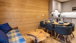 Una habitación acogedora con una pared de madera, un sofá con cojines escoceses, una mesa de comedor con sillas y una zona de cocina con armarios y electrodomésticos.