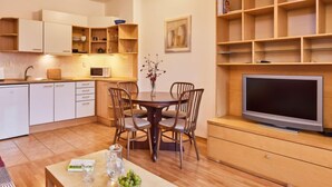 A modern kitchen with white cabinets, a dining table with chairs, a TV, and a bookshelf. - Sunlight by Interhome (Janské Lázně)