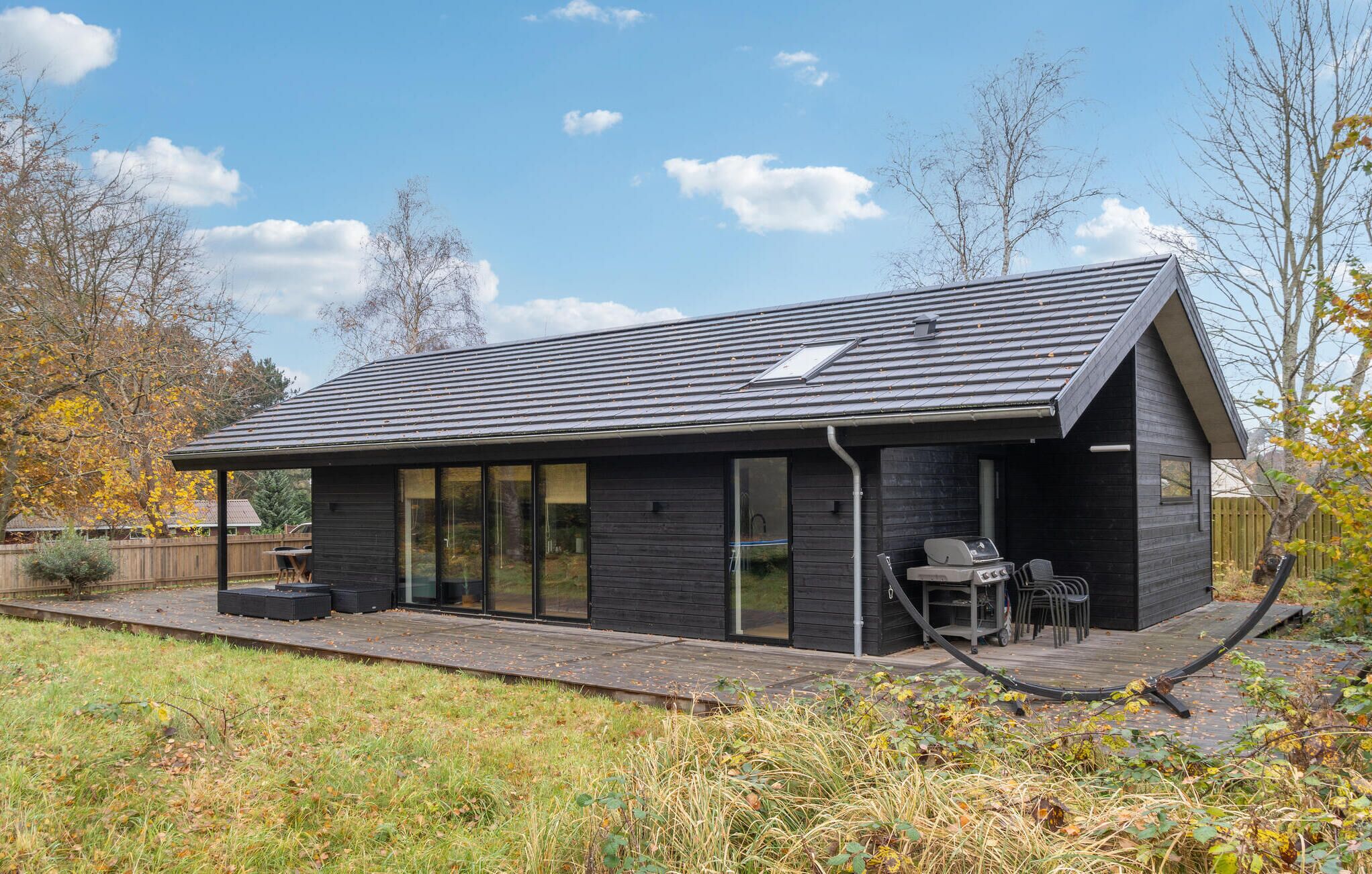 Una casa moderna con fachada oscura, ventanas grandes y un patio con mobiliario exterior.