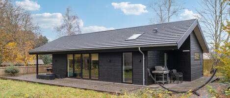 Una casa moderna con fachada oscura, ventanas grandes y un patio con mobiliario exterior.