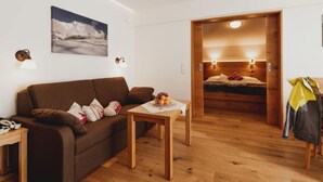 A cozy room with a brown sofa, a small wooden table with a fruit bowl, and a bed with a wooden headboard. - 2 Raum Typ Klingspitz by Interhome (Dienten am Hochkönig)