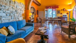Uma sala de estar acolhedora com uma parede de pedra, um sofá azul, uma mesa de centro de madeira e uma mesa de jantar com cadeiras.