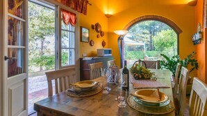 Uma sala de jantar com mesa de madeira posta para dois, lareira e vista do exterior através de uma grande janela.