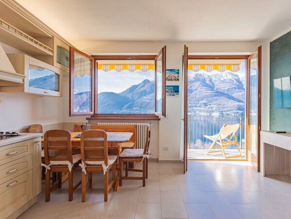 Une cuisine avec des meubles de rangement en bois, une table à manger avec des chaises, et une vue sur les montagnes par de grandes fenêtres.