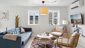 A cozy living room with a blue sofa, a round coffee table, and wicker chairs. There is a large window with a view of the outdoors, a hanging light fixture, and a wall-mounted TV. - "Elizabeta" - 175m from the sea by Interhome (Hals)