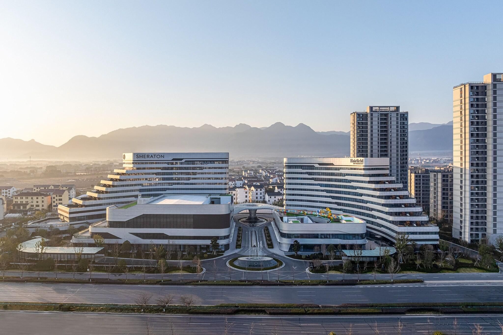 Un moderno complejo hotelero con varias edificaciones, un patio central y vistas a montañas distantes.