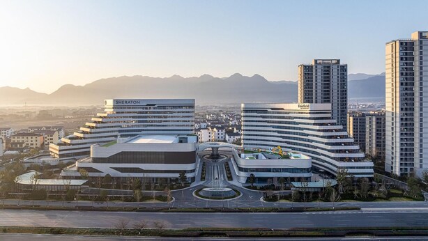Un moderno complejo hotelero con varias edificaciones, un patio central y vistas a montañas distantes.