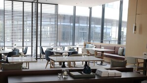 Un área de lounge moderna con disposición de asientos, mesas y grandes ventanales con vistas.
