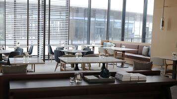 Un área de lounge moderna con disposición de asientos, mesas y grandes ventanales con vistas.