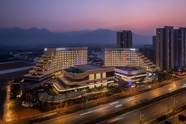 A hotel complex with multiple buildings, a parking area, and a road with moving vehicles. - Fairfield By Marriott Pujiang (Jinhua)