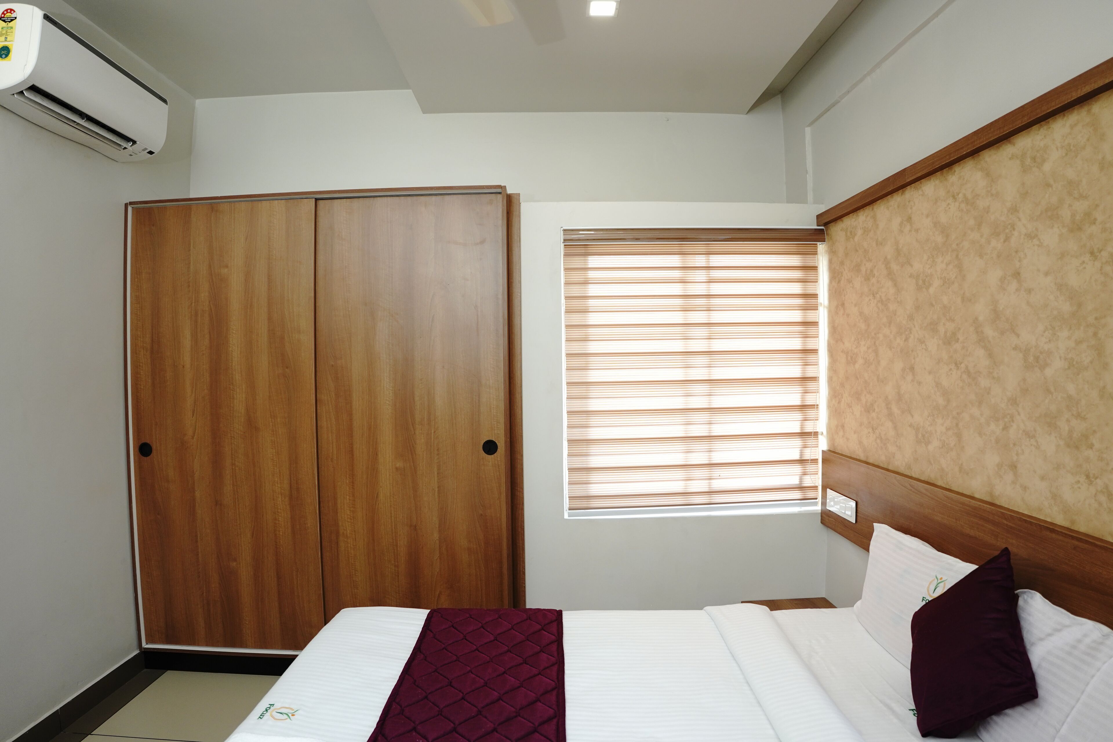 Une chambre d’hôtel avec un lit, une armoire en bois et une fenêtre avec des stores.