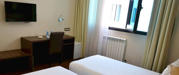 Camera d'albergo con un letto, una scrivania, una sedia, una televisione e una finestra con tende.
