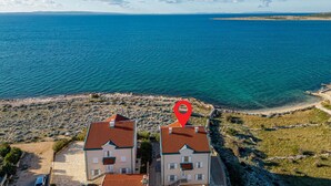 Dos edificios con techos rojos que dominan una zona costera con mar azul cristalino y un litoral rocoso.