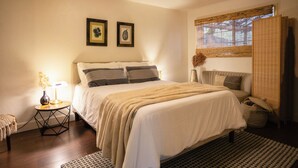 A neatly arranged bedroom with a bed, bedside tables, a lamp, and a window with blinds.