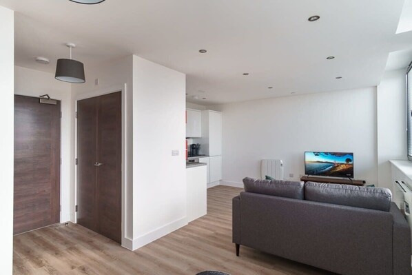 A modern living room with a grey sofa, a flat-screen TV, and a wooden floor. - Stay Zeni, Alexandra Rise Manchester Cool 1BR Flat (Manchester)