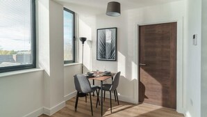 Un coin repas avec une table dressée pour deux personnes, une œuvre d’art encadrée au mur et une porte sur la droite.