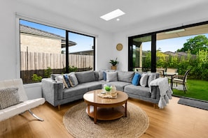 A modern living room with a grey sectional sofa, a round coffee table, and a view of a backyard through large windows.