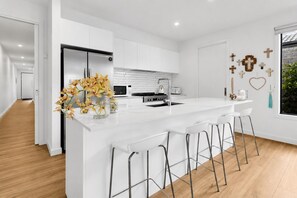 A modern kitchen with white cabinetry, a central island with bar stools, a stainless steel refrigerator, and a microwave.