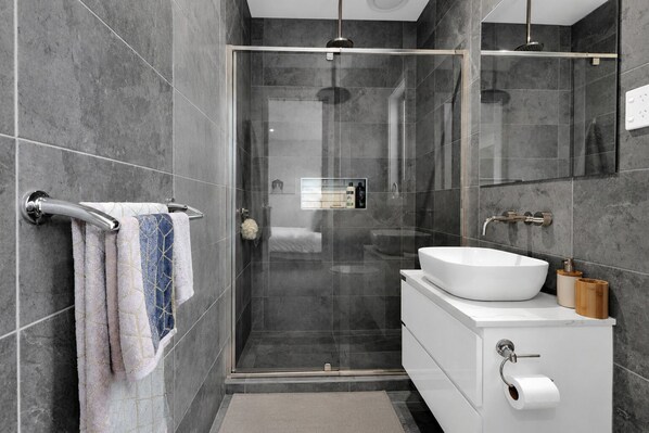 Ein modernes Badezimmer mit einer Glaskabine zur Dusche, einem weißen Waschbecken und einem Handtuchhalter mit mehreren Handtüchern.