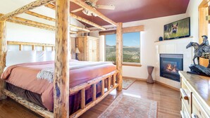 A rustic bedroom with a four-poster bed, a fireplace, and a large window offering a view of the landscape. - Great Location. Incredible Views. Clubhouse. (Silverthorne)