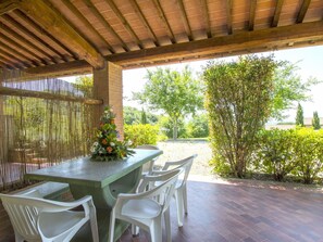 An outdoor patio with a table and chairs, a decorative floral arrangement, and a view of greenery and trees.