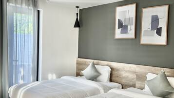 A modern bedroom with two beds, a grey accent wall, and abstract artwork.