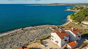 Un bâtiment situé sur la côte, doté d’un toit recouvert de tuiles rouges, et se trouvant près d’une côte rocheuse bordée d’eaux bleues et limpides.