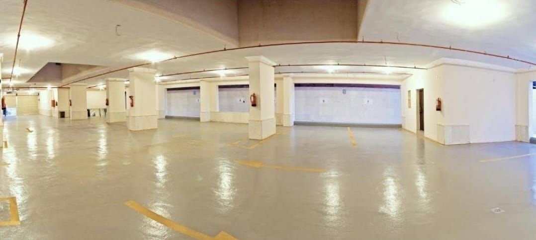 Een ruime parkeergarage binnen met veel parkeerplaatsen, witte pilaren en een schone, reflecterende vloer.