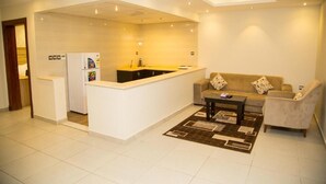 Una sala moderna con un sofá, una mesa de centro y una zona de cocina con refrigerador y lavaplatos.