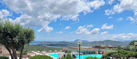 A resort with a swimming pool, lush greenery, and a view of distant mountains and water.