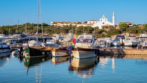 Uma marina com vários barcos atracados, uma igreja com um campanário, e edifícios ao fundo.