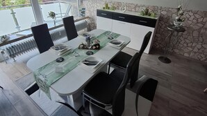 A dining area with a table set for four, black chairs, a stone accent wall, and a view of greenery outside.