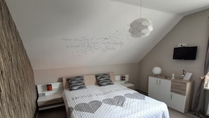 A bedroom with a bed, bedside tables, a TV, and a decorative wall.