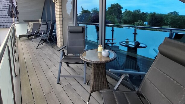 A deck with outdoor seating, a glass table, and a view of a body of water.