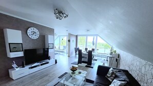 A modern living room with a flat-screen TV, a sofa, and a dining area with a table and chairs.