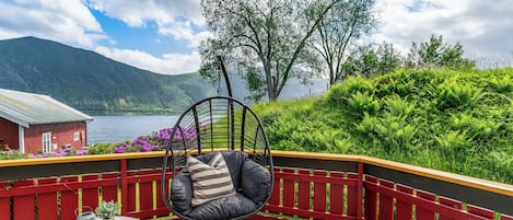 A wooden deck with a hanging chair, a small table with potted plants, and a red railing.