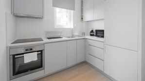 Une cuisine moderne avec des meubles blancs, un four encastré, un micro-ondes et une fenêtre qui laisse entrer la lumière naturelle.