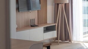 Une chambre d’hôtel moderne dotée d’un téléviseur à écran plat fixé sur un panneau mural en bois, d’un bureau avec une chaise et d’une lampe sur pied.