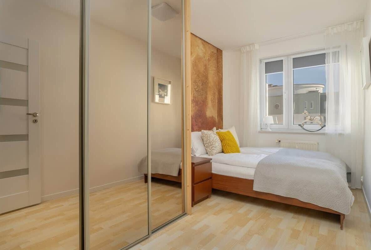 A bedroom with a bed, bedside tables, a mirror, and a window with curtains.