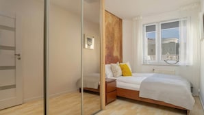 A bedroom with a bed, bedside tables, a mirror, and a window with curtains. - Functional Apartment in Poznan | Place to Work (Poznan)