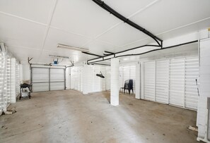 An empty garage with white doors, a concrete floor, and black pipes on the ceiling.