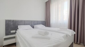 Un lit bien fait, avec du linge de lit blanc et une serviette pliée, une table de chevet et une fenêtre avec des rideaux.