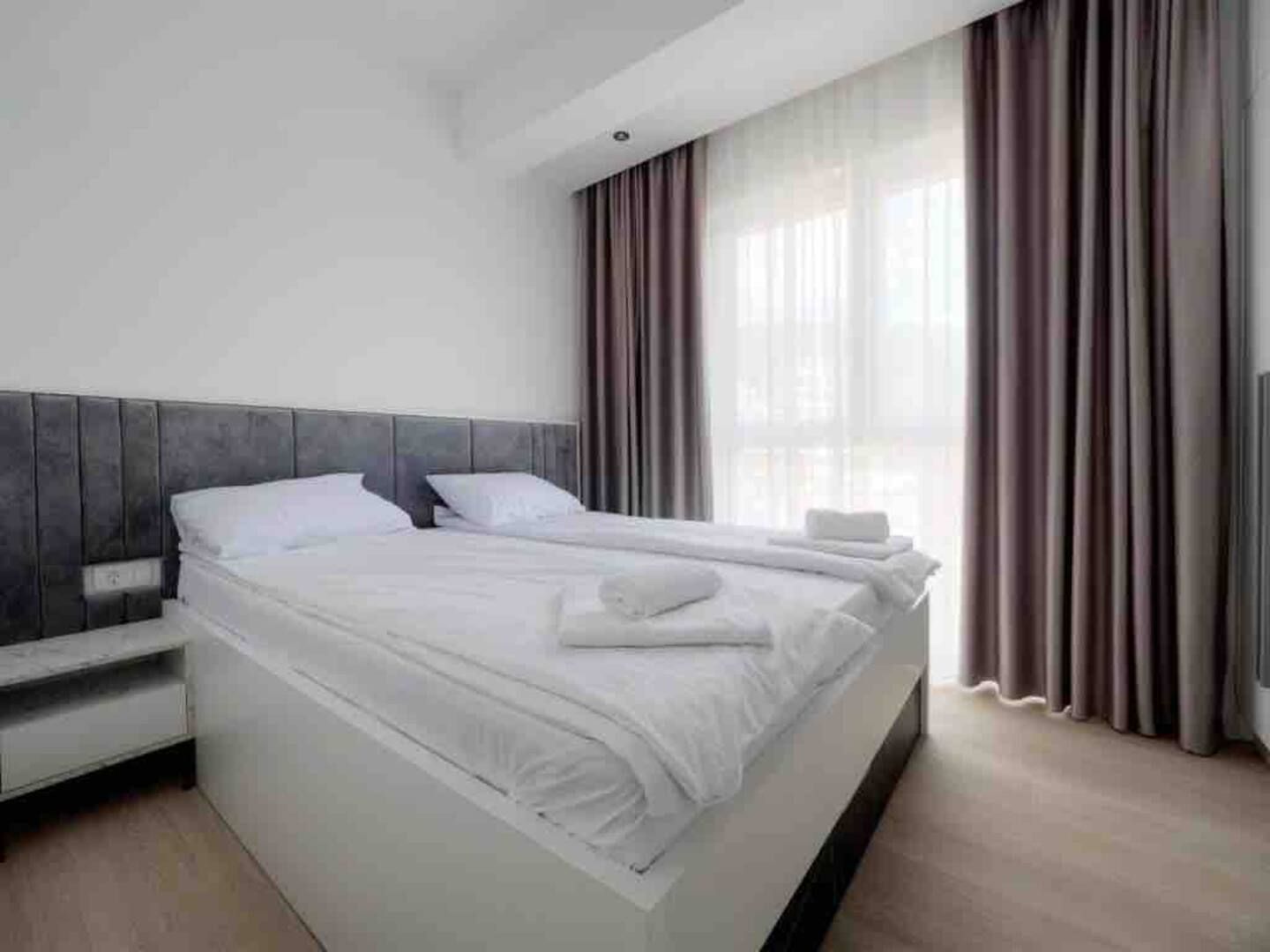 Una habitación de hotel moderna con una cama grande, una mesita de noche y un ventanal con cortinas.