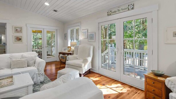 A room with a white sofa, a chair, a wooden floor, and a large window with a view of greenery.